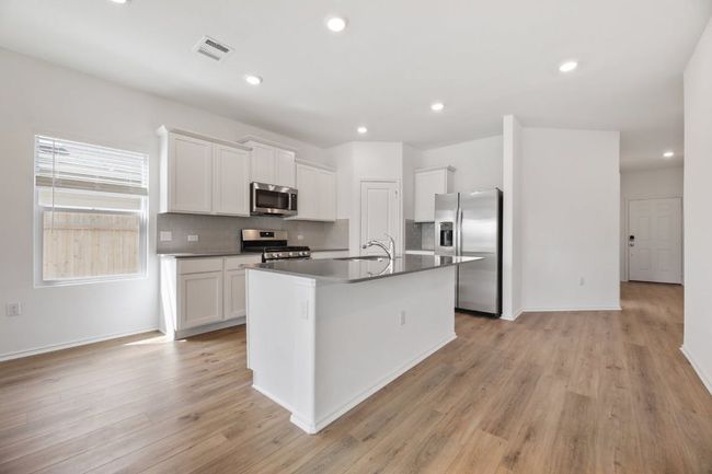 Kitchen featuring stainless steel appliances, decorative backsplash, an island with sink, white cabinets, and dark countertops | Image 13
