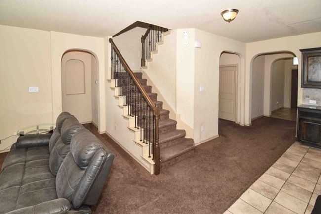 Unfurnished living room with arched walkways, stairs, carpet flooring, tile patterned floors, and baseboards | Image 14