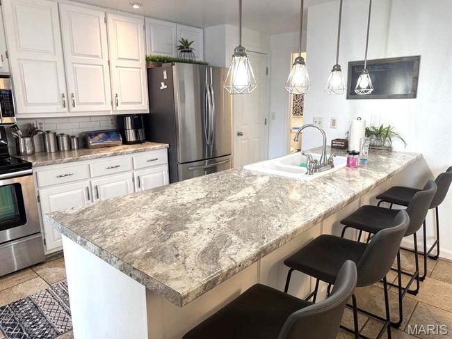 Kitchen featuring appliances with stainless steel finishes, a sink, white cabinets, tasteful backsplash, and a breakfast bar area | Image 15