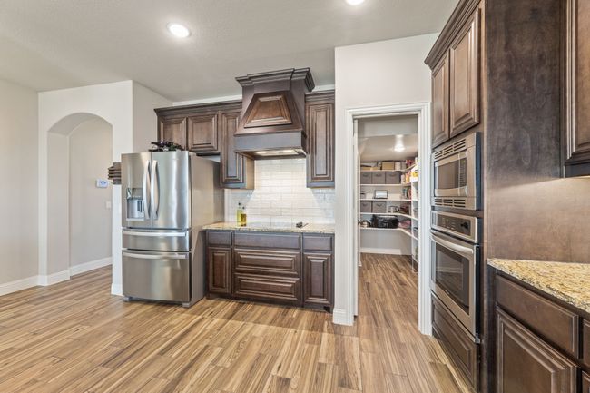 Kitchen featuring appliances with stainless steel finishes, light wood-style floors, premium range hood, dark brown cabinetry, and recessed lighting | Image 8