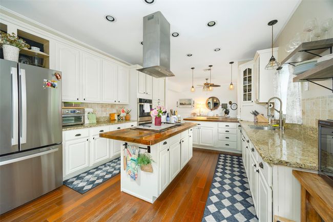 Kitchen featuring stainless steel appliances, butcher block countertops, a sink, island exhaust hood, and tasteful backsplash | Image 7