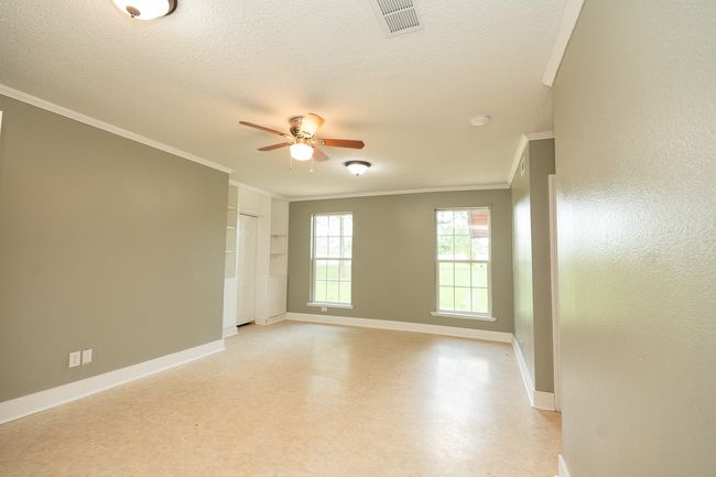 Spare room featuring crown molding, a ceiling fan, light flooring, a textured ceiling, and built in shelves | Image 28