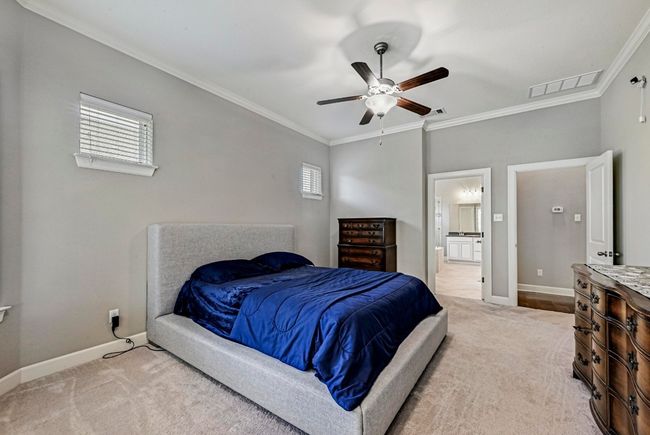 Bedroom with light colored carpet, ornamental molding, multiple windows, connected bathroom, and a ceiling fan | Image 16
