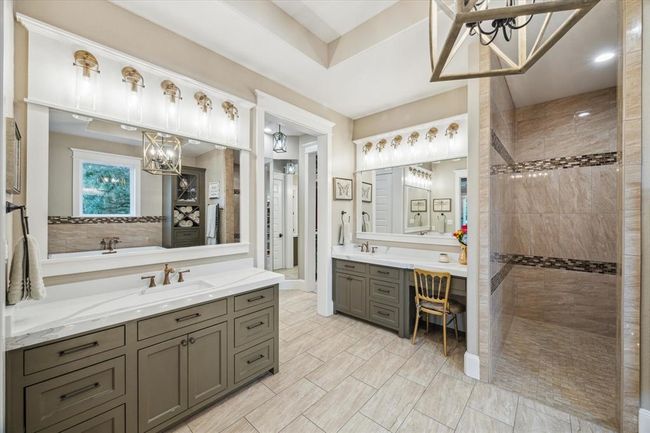 The primary bathroom is thoughtfully designed with two separate custom vanities and a dedicated makeup vanity, all framed by elegant custom crown molding around the mirrors. The space is further enhanced with tailored lighting, providing both functionality and a refined touch of luxury. | Image 19