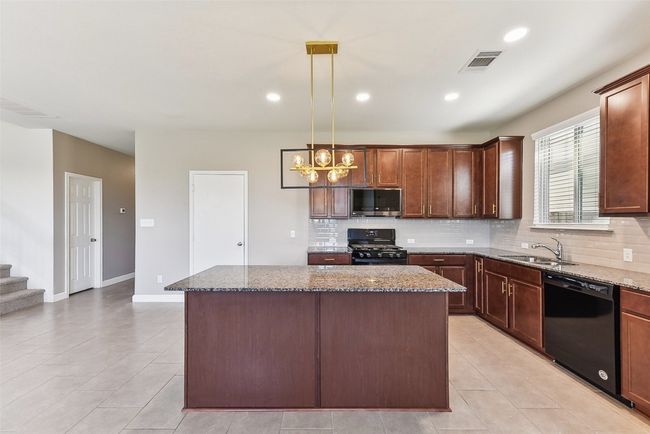Kitchen with dark stone countertops, visible vents, backsplash, and black appliances | Image 8
