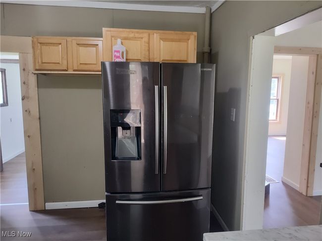 Kitchen featuring stainless steel fridge with ice dispenser, light brown cabinetry, dark wood-type flooring, and baseboards | Image 22