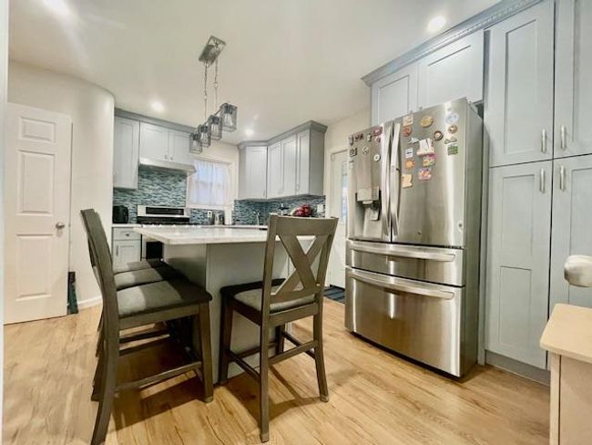 Kitchen featuring stainless steel appliances, light countertops, decorative backsplash, light wood finished floors, and a kitchen bar | Image 5