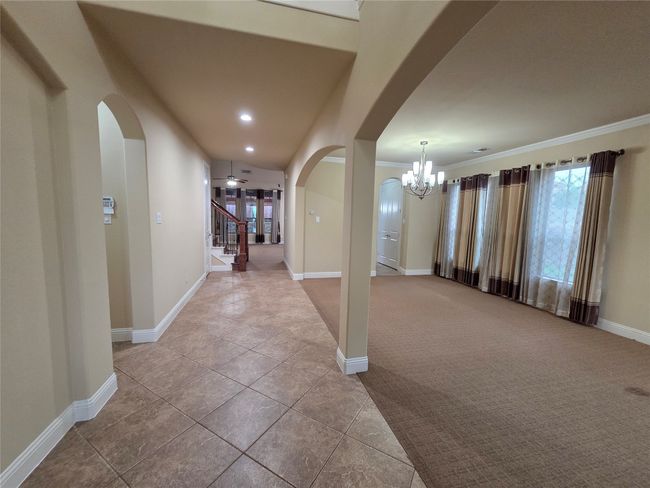 Tiled foyer entrance featuring arched walkways, a chandelier, ornamental molding, carpet floors, and stairway | Image 9