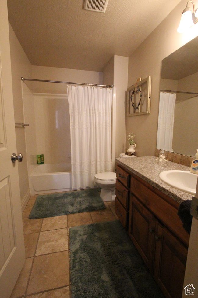 Bathroom with visible vents, toilet, shower / tub combo with curtain, a textured ceiling, and vanity | Image 10