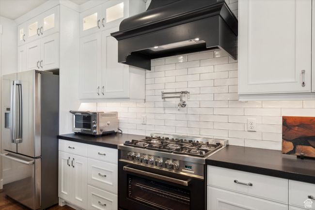 Kitchen with dark countertops, white cabinets, appliances with stainless steel finishes, and under cabinet range hood | Image 18