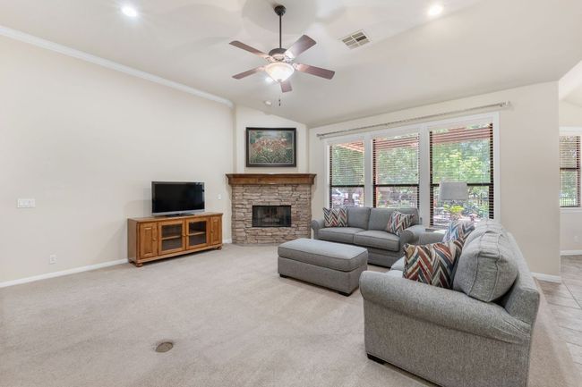 Living room featuring ceiling fan, lofted ceiling, a stone fireplace, light carpet, and ornamental molding | Image 7