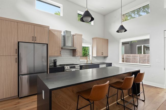 Kitchen with stainless steel appliances, wall chimney exhaust hood, a high ceiling, dark countertops, and a kitchen breakfast bar | Image 8