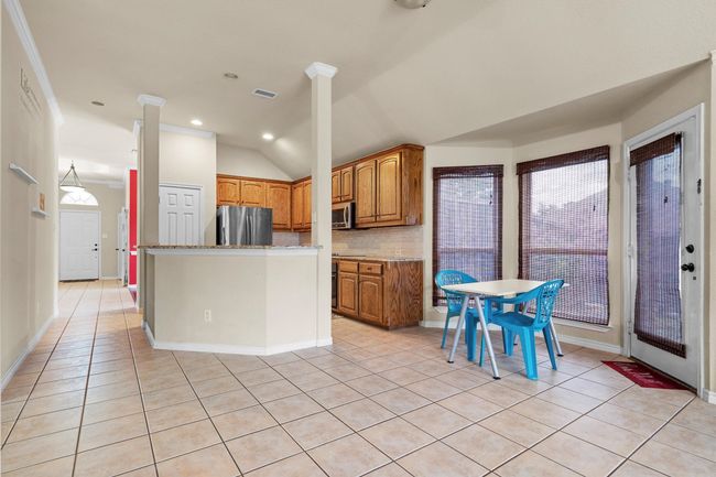 Kitchen featuring appliances with stainless steel finishes, decorative backsplash, brown cabinets, light tile patterned flooring, and vaulted ceiling | Image 12
