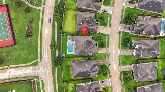 This aerial photo showcases a suburban neighborhood with well-maintained homes, each featuring spacious yards. Our highlighted property has a backyard pool, covered patio and nearby is a tennis court, providing a glimpse of community amenities. The area is lush and green, with wide streets and ample parking. | Image 48