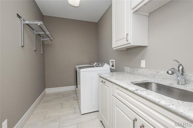 First floor laundry featuring light tile patterned floors, a sink, baseboards, washer and dryer, and cabinet space | Image 17
