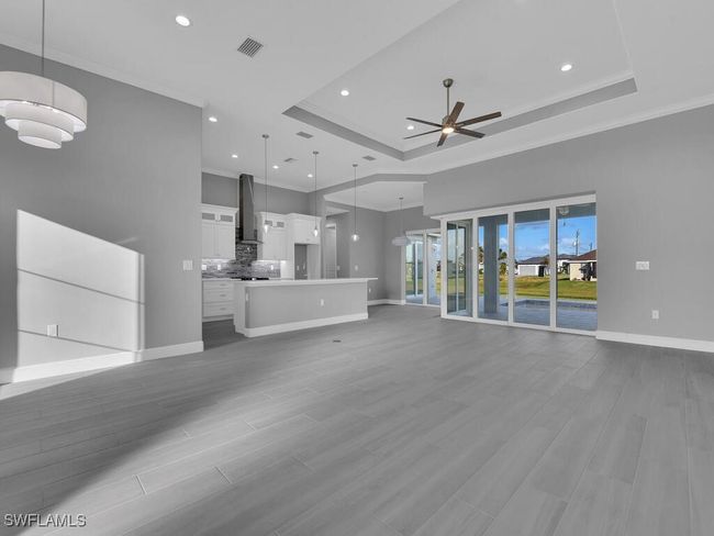 Unfurnished living room featuring ceiling fan, ornamental molding, a tray ceiling, recessed lighting, and wood finished floors | Image 7