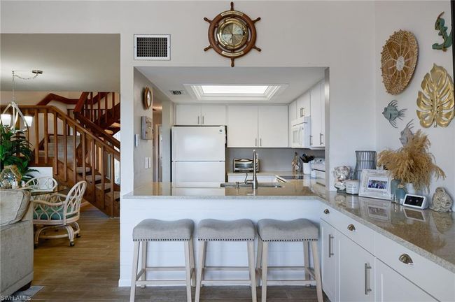 Kitchen with a kitchen bar, white cabinetry, light stone counters, kitchen peninsula, and white appliances | Image 7