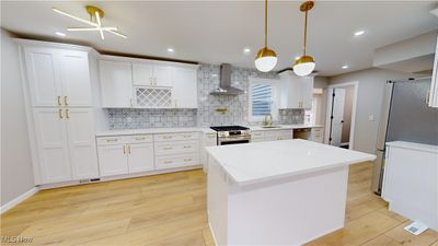 Kitchen featuring white cabinets, wall chimney range hood, sink, appliances with stainless steel finishes, and light hardwood / wood-style floors | Image 3