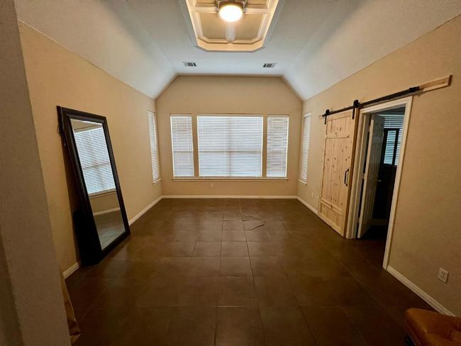 Spare room featuring dark tile patterned flooring, lofted ceiling, and a barn door | Image 9