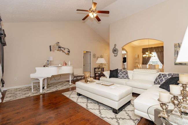 Living area featuring high vaulted ceiling, hardwood / wood-style floors, ceiling fan with notable chandelier, arched walkways, and baseboards | Image 5
