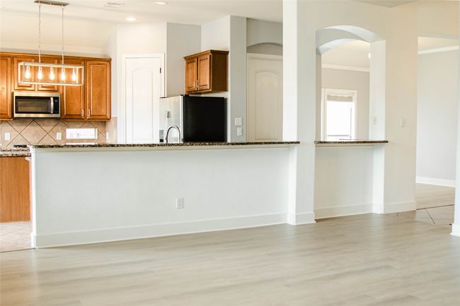 Kitchen featuring appliances with stainless steel finishes, dark stone counters, light wood-style flooring, brown cabinets, and arched walkways | Image 11
