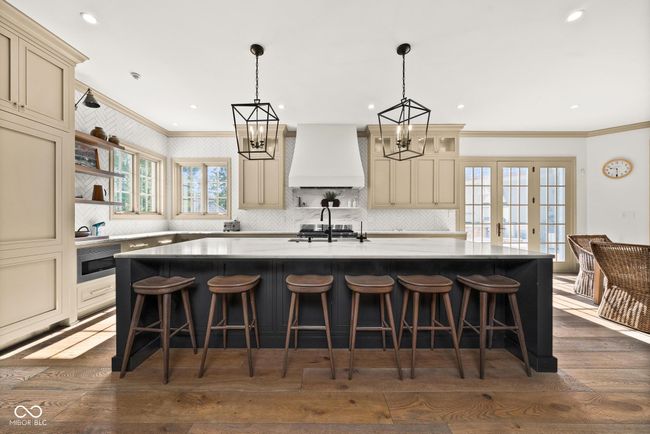 kitchen with custom range hood, ornamental molding, cream cabinetry, a kitchen island with sink | Image 15