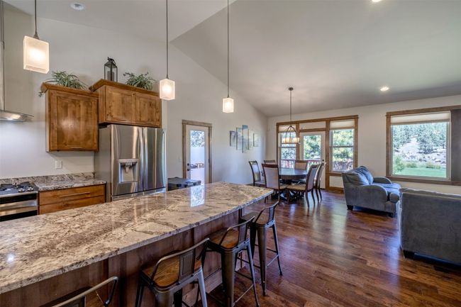 Kitchen featuring appliances with stainless steel finishes, dark wood-type flooring, brown cabinets, a breakfast bar, and light stone counters | Image 13