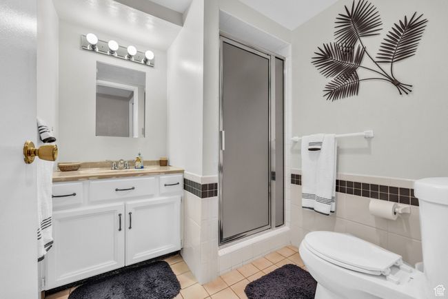 Bathroom with toilet, tile patterned floors, tile walls, vanity, and a shower stall | Image 22