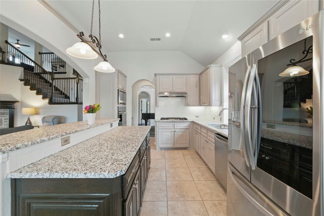 Kitchen with appliances with stainless steel finishes, under cabinet range hood, arched walkways, a center island, and light stone countertops | Image 12