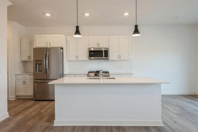 Photo is of the actual home. The spacious kitchen features a large center island, quartz countertops, recessed lighting, under mount sink, LVP floors, stainless appliances and more! | Image 2