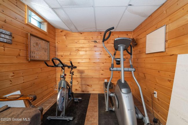 Basement finished area currently used as a cardio room featuring natural wood paneling and ceramic tile flooring | Image 37