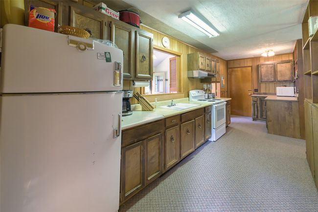 Kitchen featuring white appliances, under cabinet range hood, light countertops, wooden walls, and carpet floors | Image 16