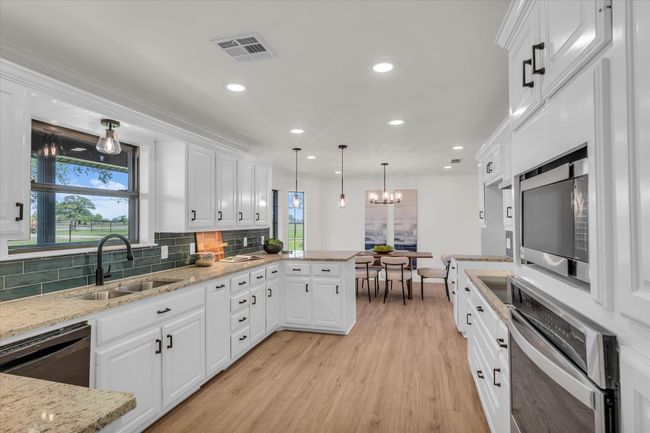 Kitchen featuring a peninsula, white cabinetry, visible vents, a sink, and stainless steel appliances | Image 19