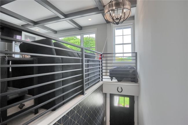 Sleek metal railings and a statement chandelier elevate the landing, offering a dramatic view of the living area’s coffered ceiling and oversized windows that frame the lush outdoor scenery. | Image 6