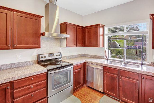 Kitchen with appliances with stainless steel finishes, wall chimney range hood, reddish brown cabinets, light countertops, and light wood-style floors | Image 12
