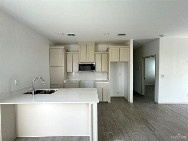 Kitchen featuring stainless steel microwave, dark wood-style flooring, visible vents, and a sink | Image 4