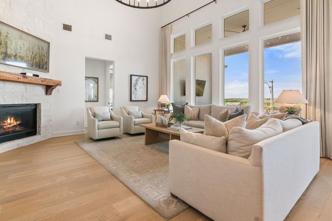 Living area with light wood-style floors, a fireplace, a towering ceiling, and a chandelier | Image 7