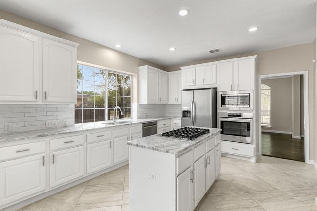 Kitchen featuring a sink, a kitchen island, stainless steel appliances, white cabinets, and decorative backsplash | Image 11