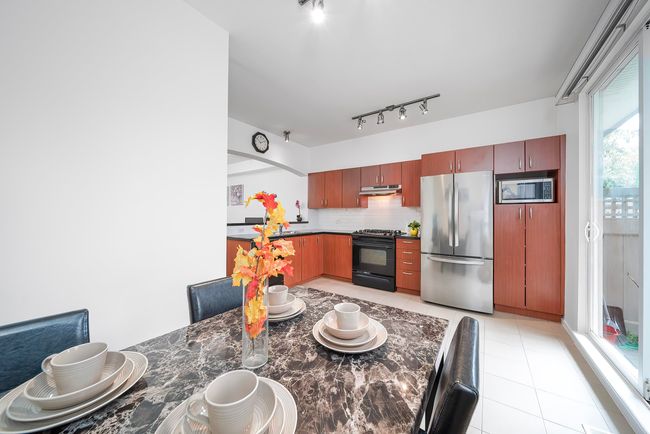 Kitchen with light tile patterned floors, backsplash, dark countertops, under cabinet range hood, and appliances with stainless steel finishes | Image 13