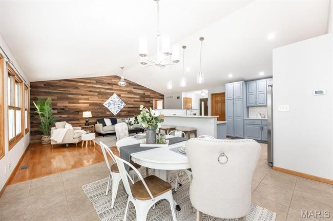 Dining area featuring wooden walls, vaulted ceiling, a chandelier, light tile patterned floors, and baseboards | Image 16