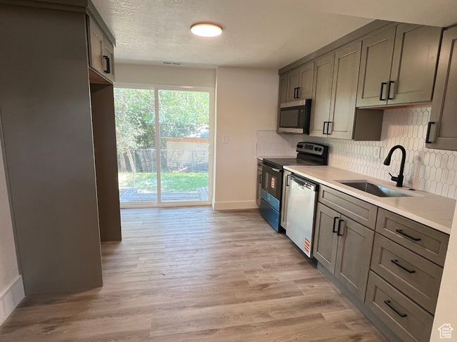 Kitchen with stainless steel appliances, decorative backsplash, light wood-type flooring, light countertops, and a textured ceiling | Image 14