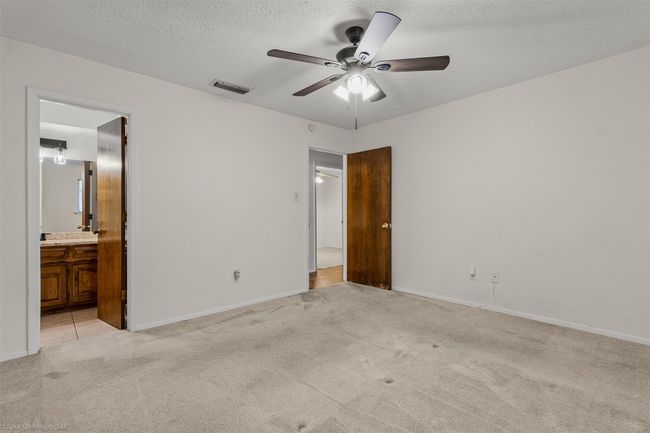 Unfurnished bedroom with light colored carpet, a textured ceiling, ensuite bath, baseboards, and ceiling fan | Image 18