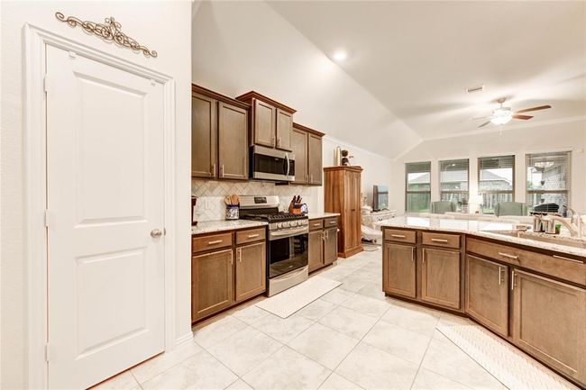 Open concept kitchen with dark wood cabinets, farmhouse sink, gas stovetop and oven, granite countertops, and pantry | Image 11