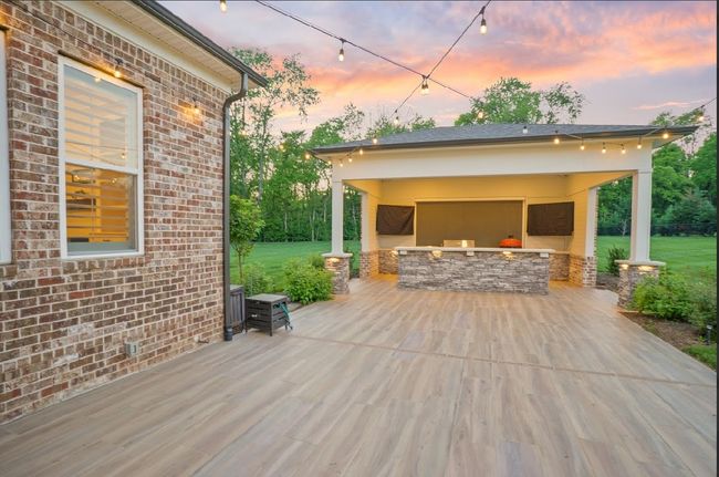 This stunning outdoor kitchen pavilion with string lights, stone finishes, and ample space is the perfect setup for hosting under the sunset sky. | Image 7