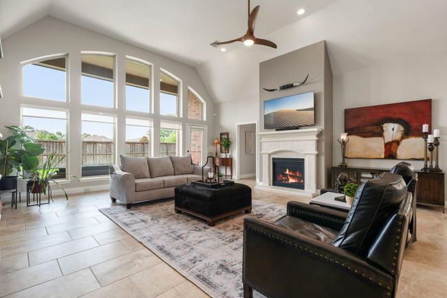 This living room is more like a GREAT room featuring a stunning fireplace with mantel detailing, custom neutral paint, soaring high ceiling, recessed lighting, custom ceiling fan, and an amazing wall of windows providing a lovely view of your backyard to keep an eye out on the kids or pets playing. | Image 4