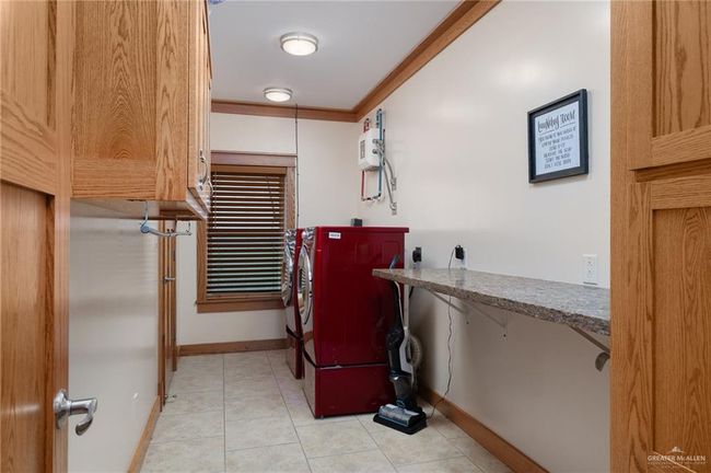 Clothes washing area featuring light tile patterned floors, crown molding, and washing machine and clothes dryer | Image 16