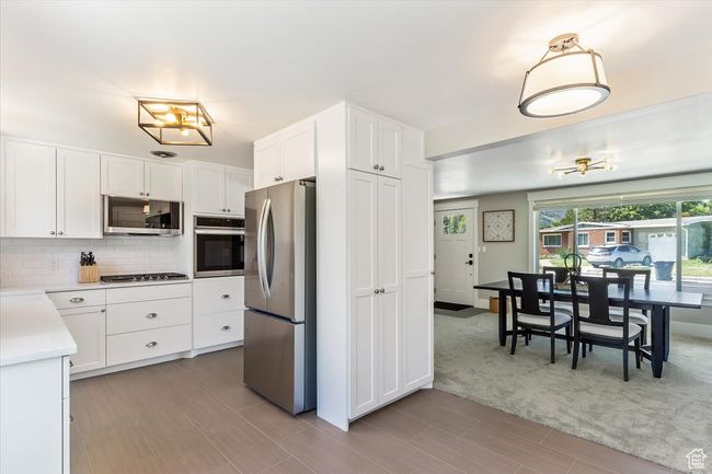 Kitchen featuring appliances with stainless steel finishes, light countertops, decorative backsplash, white cabinets, and light wood finished floors | Image 19