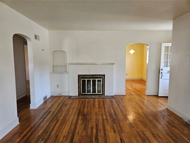 Unfurnished living room featuring a fireplace with flush hearth, visible vents, baseboards, arched walkways, and wood finished floors | Image 9
