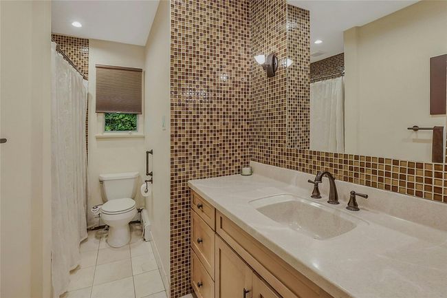 Bathroom with toilet, vanity, tile walls, tile patterned flooring, and a shower with curtain | Image 22