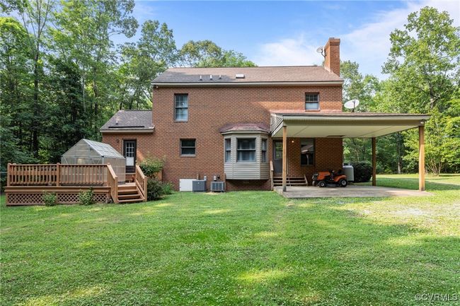 Rear view of house featuring a greenhouse, a chimney, brick siding, a yard, and an attached carport | Image 36